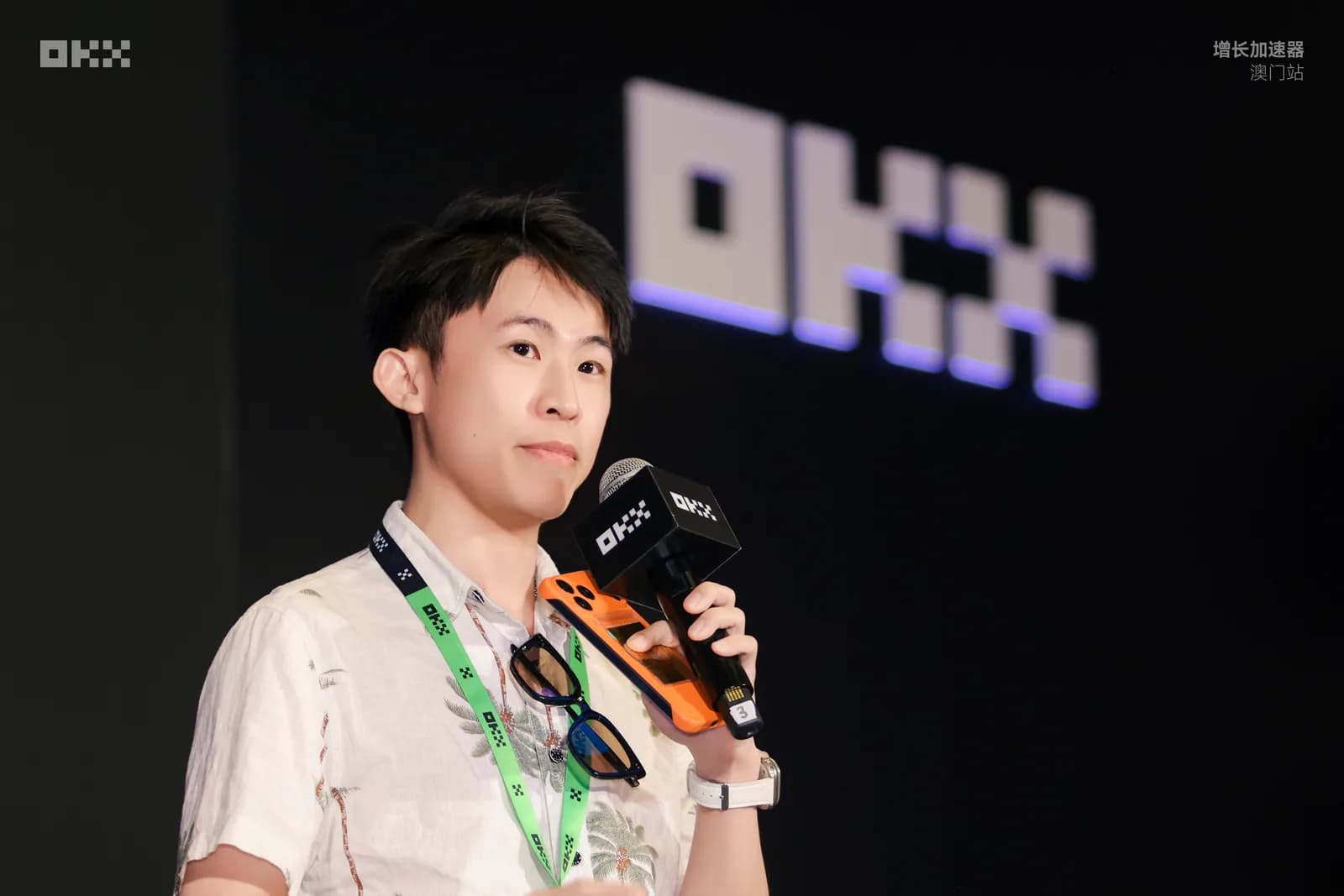 氣球柯男在 OKX 增長加速器澳門站舞台上手持 OKX 麥克風演講