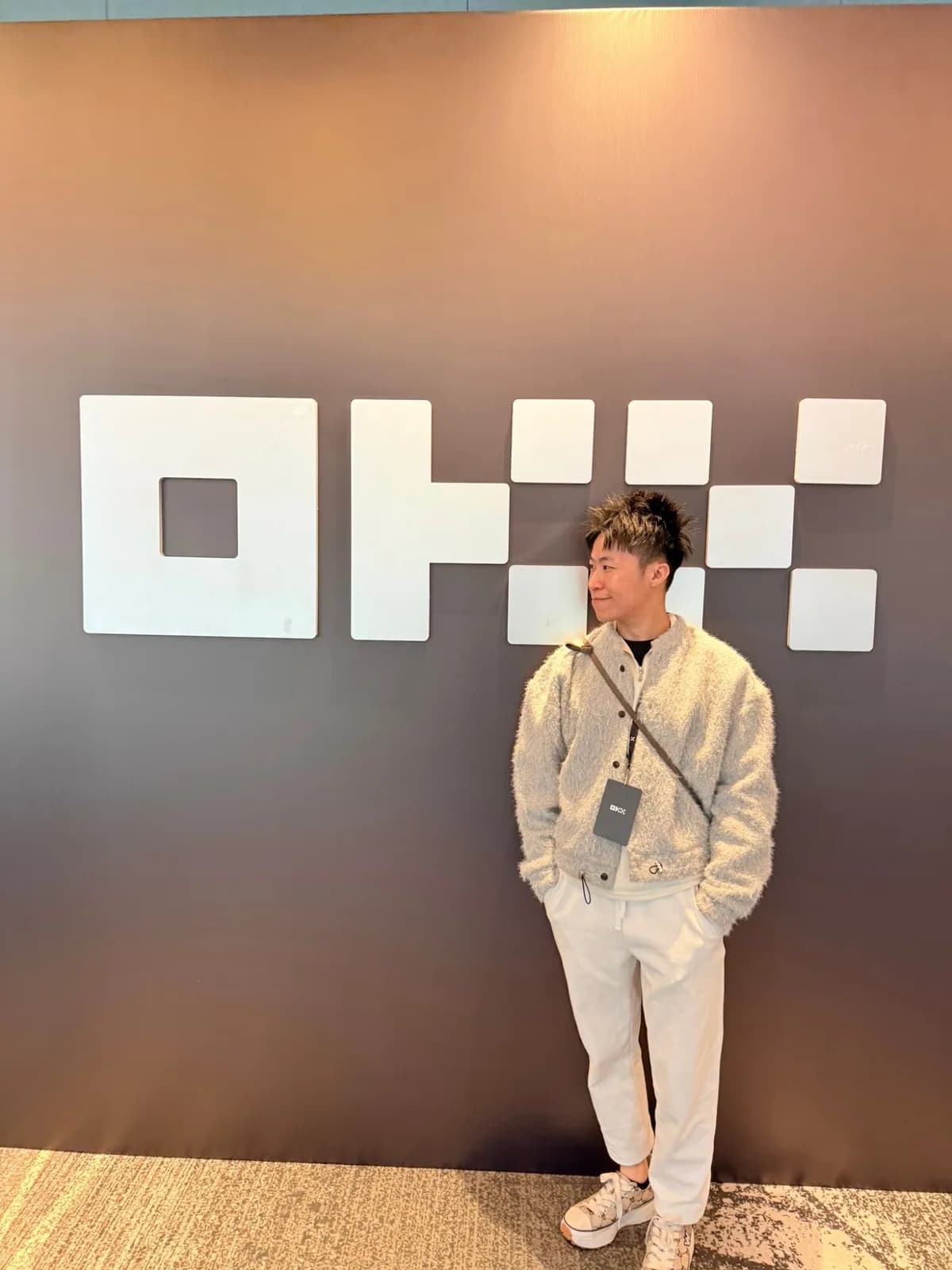 氣球柯男在 OKX 品牌牆前留影,掛 OKX 識別證